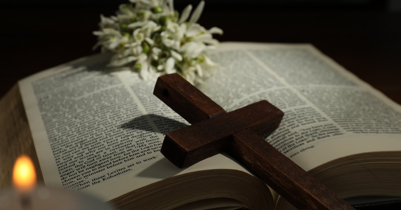 Cross, Bible, flowers and church candle on wooden table